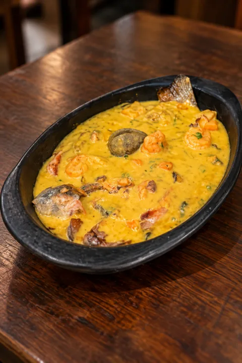 Trucha en salsa marinera servida en cazuela negra, con camarones y mariscos en salsa cremosa amarilla